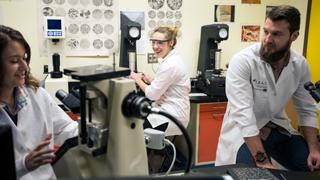 三个学生正在实验室里研究显微镜. 右边的学生在说话，而另外两个在看着她. 